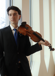 Charlie posing with his violin in front of sunny windows