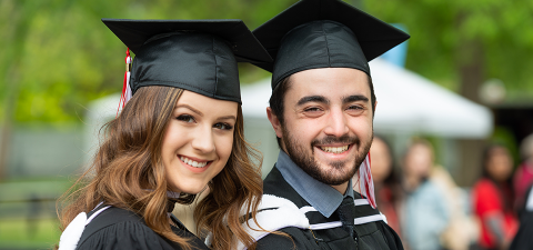 Photo of young man and young woman standing together and smiling on graduation day 