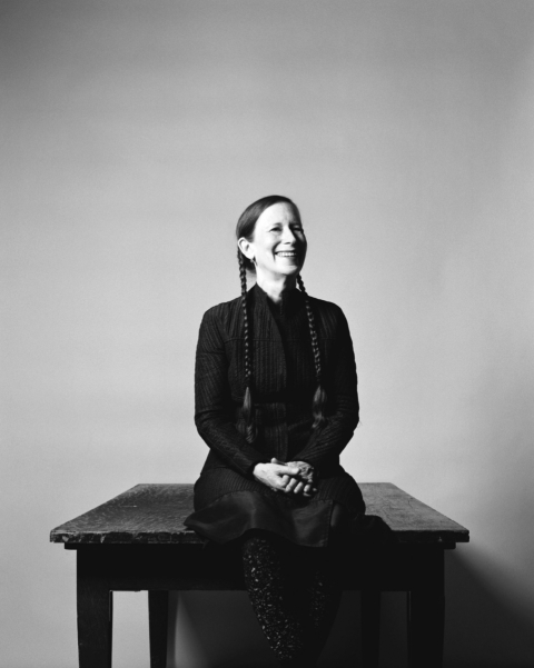 Meredith Monk sitting on a bench while smiling.