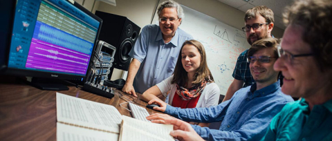 Students standing next to seated professor