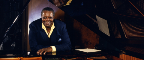 Oscar Peterson leaning on his piano with an open lid