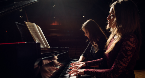Two female pianists playing a piano