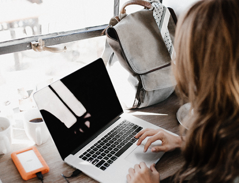 woman typing on laptop with backpack nearby