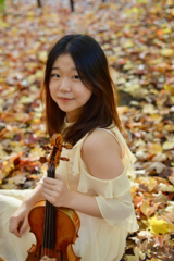 Juan Lee sitting in fall coloured leaves with violin