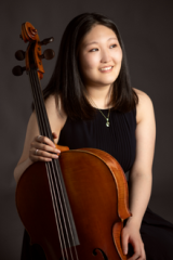 Solina Lee sitting behind a cello with gray background