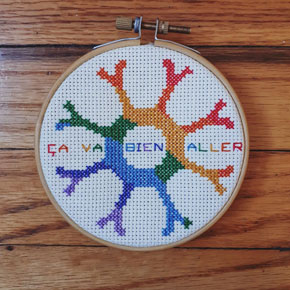 The cross stitch made by Marina Saunders featuring a rainbow version of our logo.