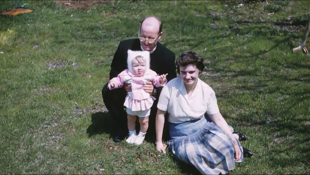 Two parents on lawn holding infant Angela Genge in costume