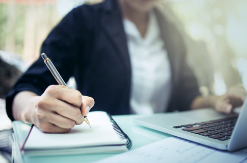 A person writing on a note book and typing on a computer