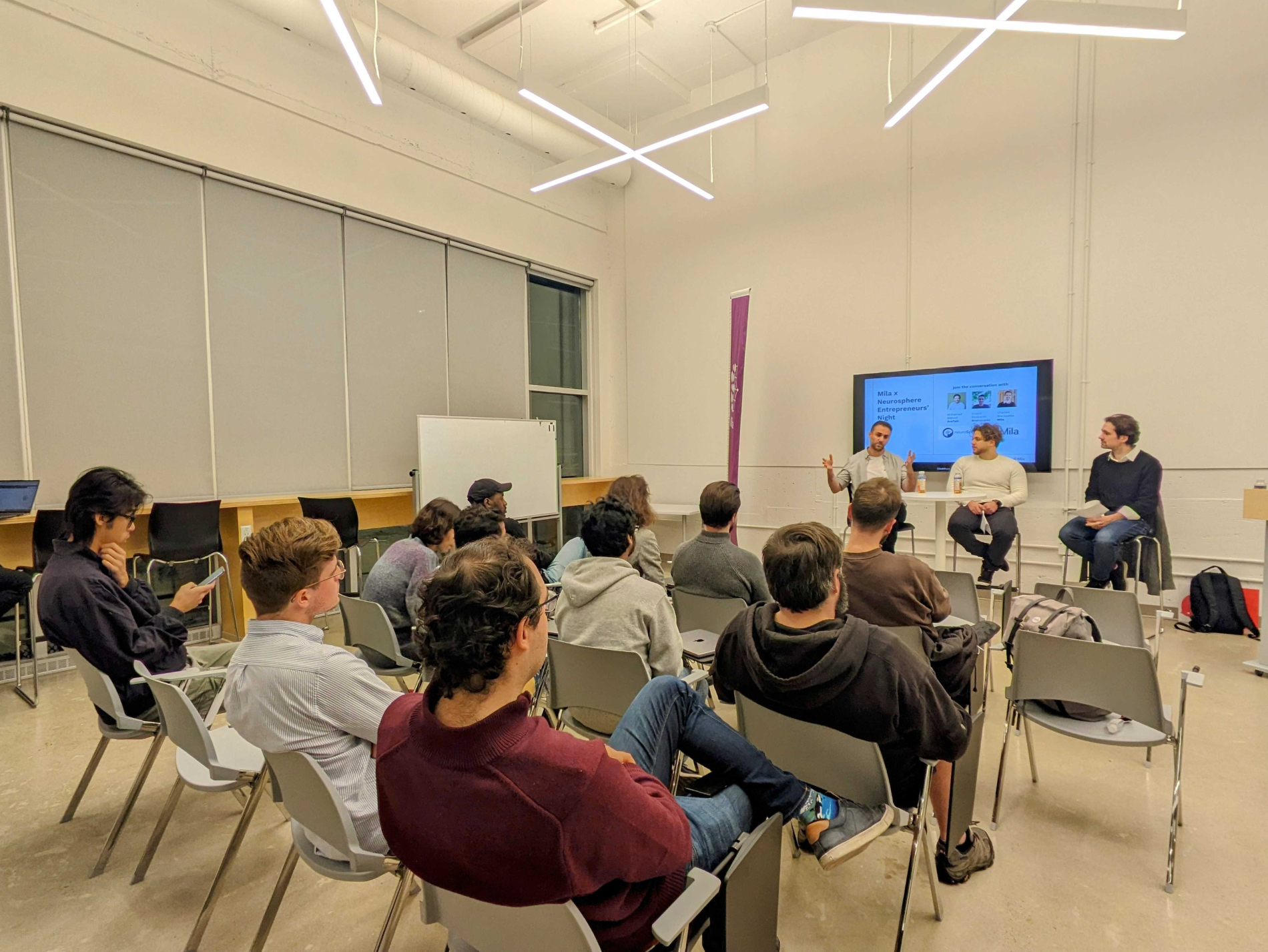 Image of attendees of the event while listening to the speakers who are on a podium with a screen behind them