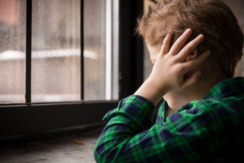 A boy facing a window rests his elbows on the windowsill 