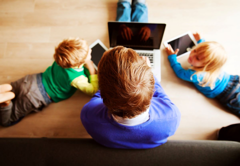 Family using digital devices together at home. / Membres d'une même famille utilisant des appareils numériques ensemble à la maison.