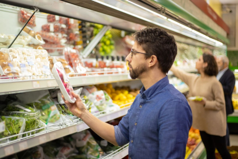 Man looking at vegetables in grocery store. / Un homme devant des légumes dans une épicerie