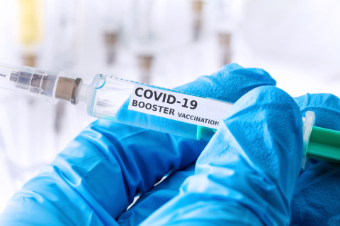 A gloved hand holds a syringe with a COVID-19 booster vaccine