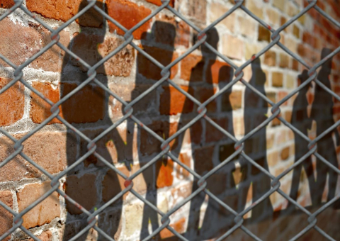 Shadows of people on a wall behind a fence.