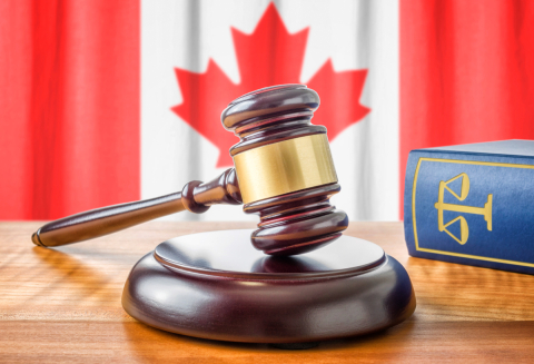 Law and justice of Canada concept with a 3d rendering of a gavel on a wooden desktop and the Canadian flag on background.