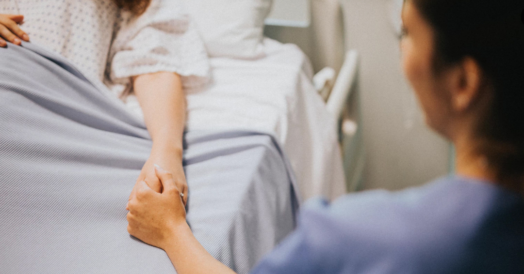 Nurse seated at the bedside holds patient's hand