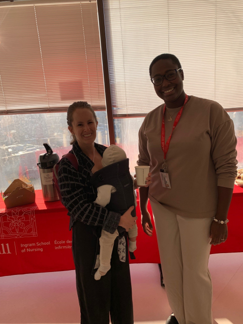 Alumni with baby in baby carrier chats with assistant lab director.