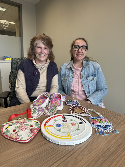 Heather Hart and Erin Patton admiring several pieces of beading Erin has done since the end of the course including a pair of mocassins.