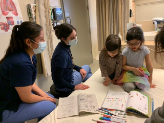 Two nursing students chat with two sisters as they colour pictures in a colouring book.