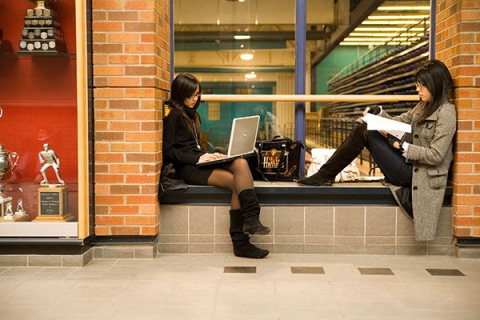 two students  studying and sitting on a window sill inside a building