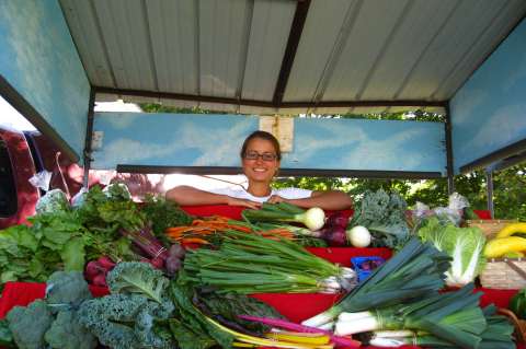 student behind vegetable display at farmer's market