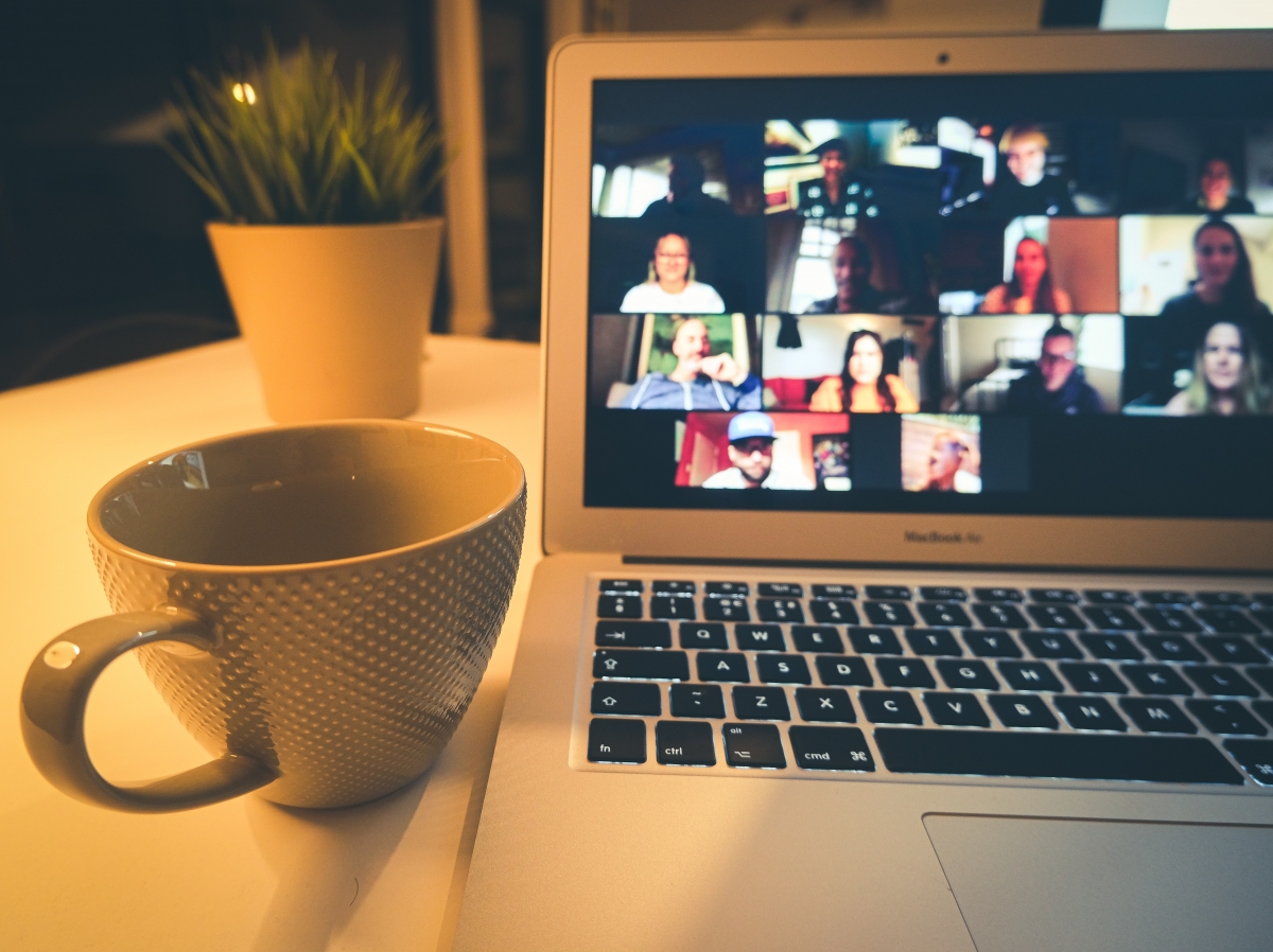 Coffee cup sits beside laptop with screen showing several participants on a video call