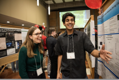 Two people smiling, looking at a poster