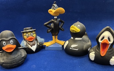 Assortment of toy ducks made of black plastic in front of a blue background.