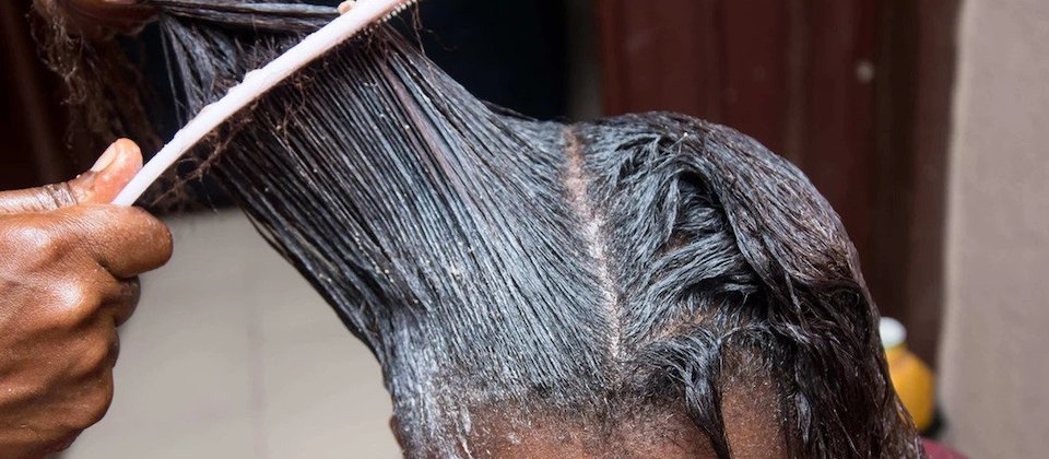 Person combing chemical straightener out of long dark hair.
