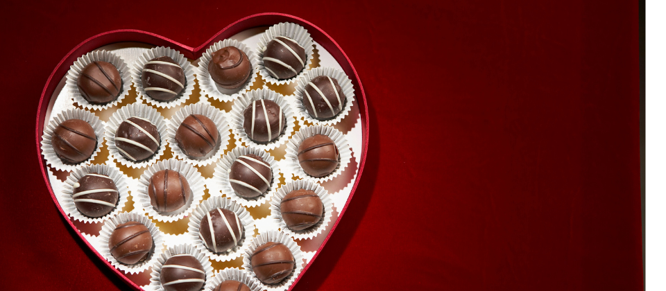Heart-shaped box of chocolates over red backdrop.