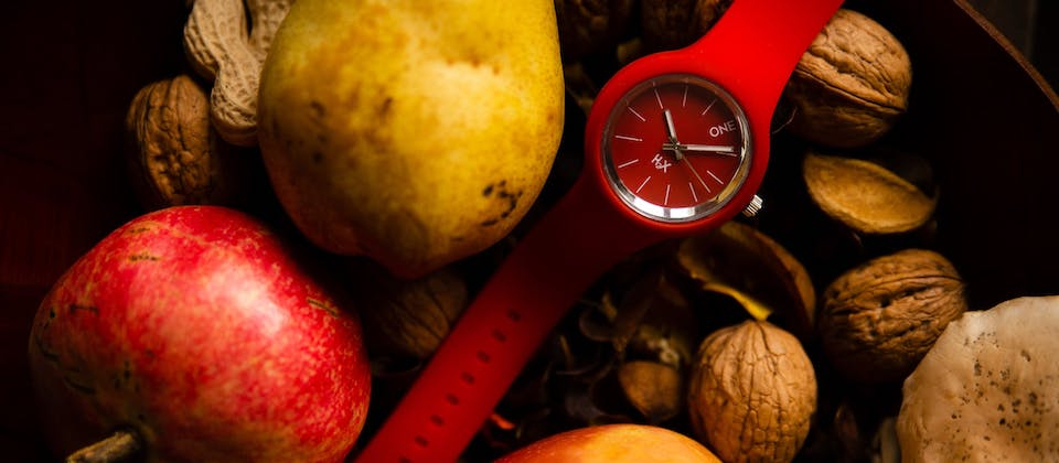 Stylish red wristwatch placed in basket with fresh fruits and vegetables