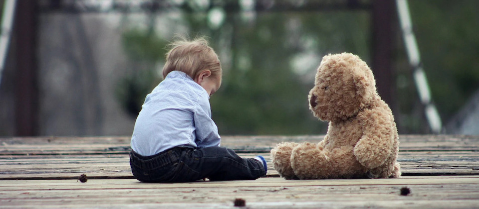 kid sitting on ground next to teddy bear