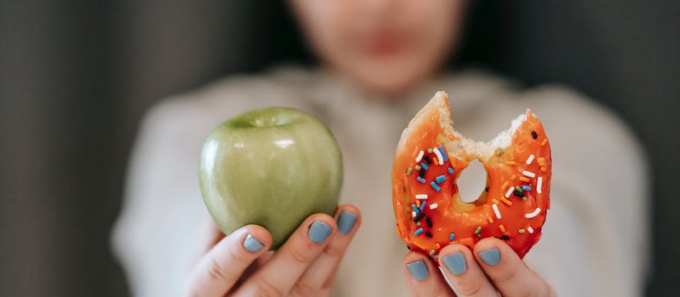 close up of a person holding up an apple next to a bitten donut
