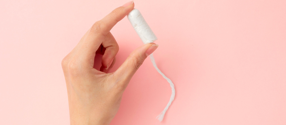 Hand holding a tampon against a pink background