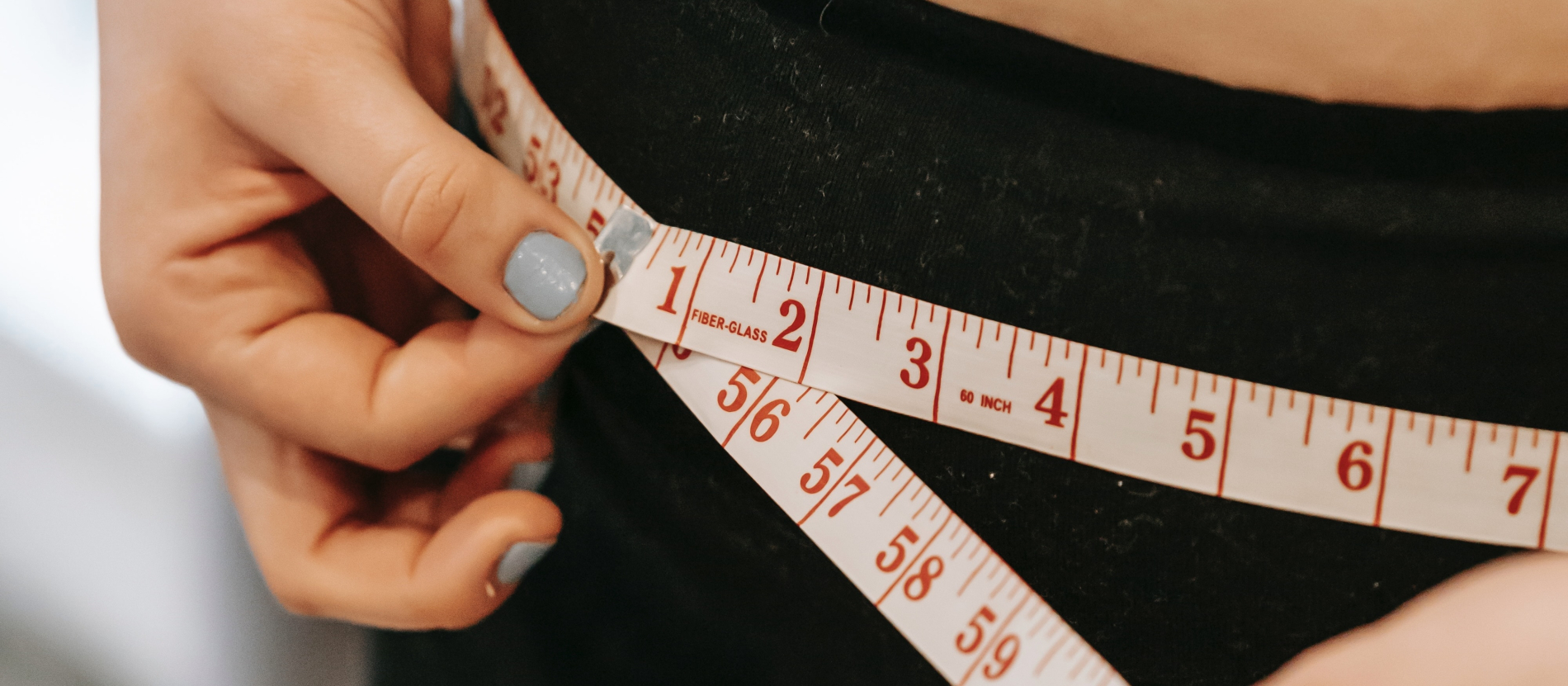 Person with blue painted nails wrapping a tape measure around their waist.