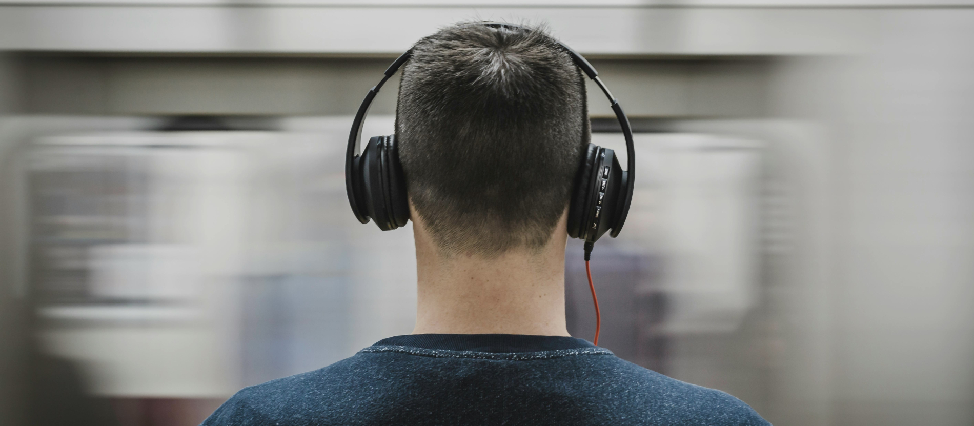 Man wearing black headphones standing in front of moving subway.