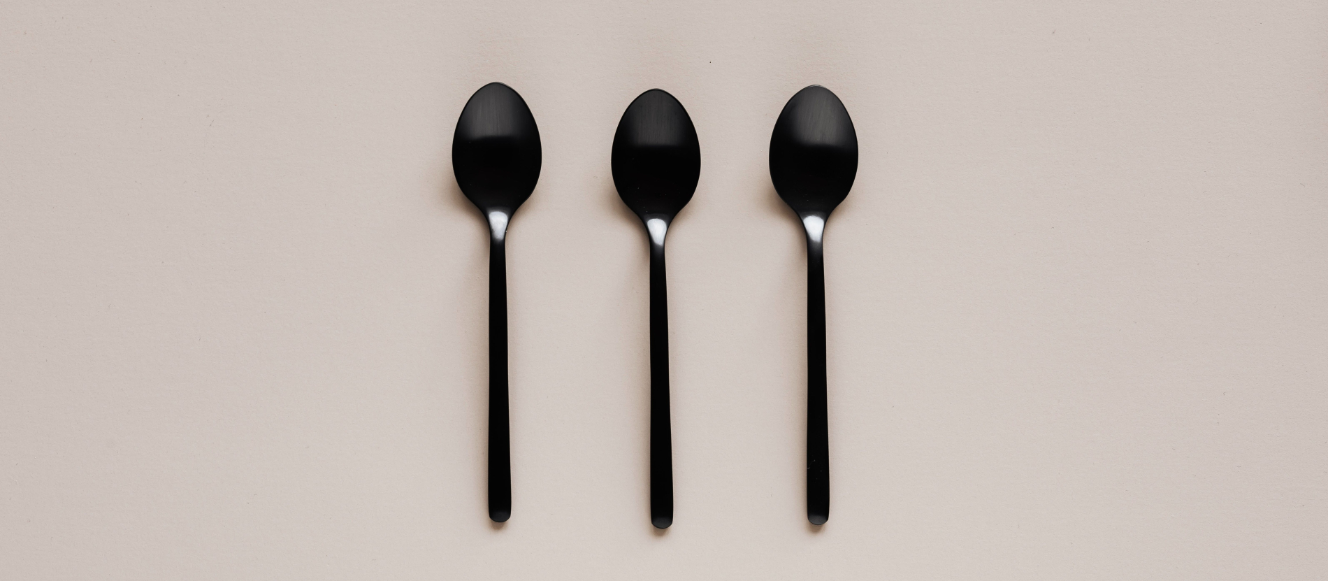 Three black, plastic spoons lined up side-by-side on a beige background.
