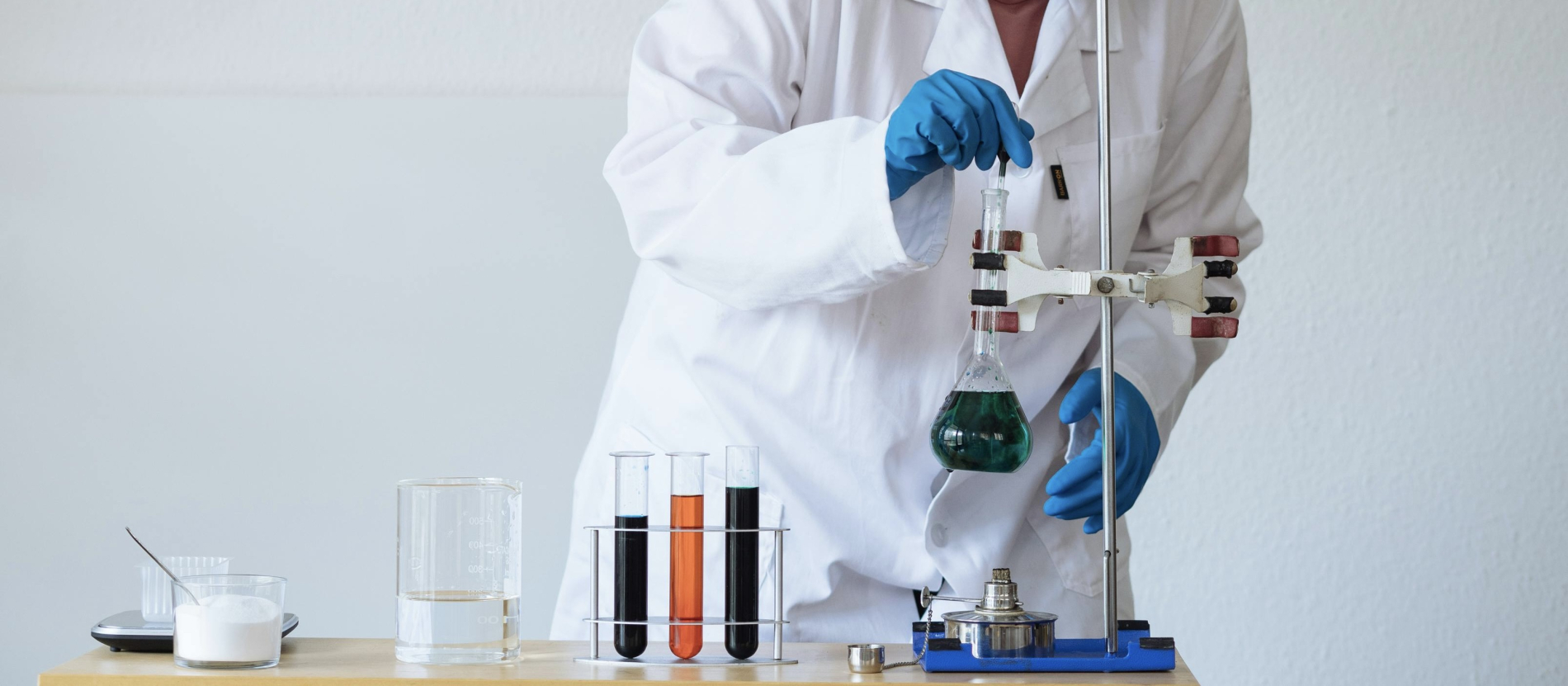 Scientist in lab coat mixing various coloured solutions.