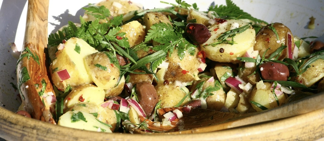 A bowl of potato salad with herbs, olives, and chopped red onions.
