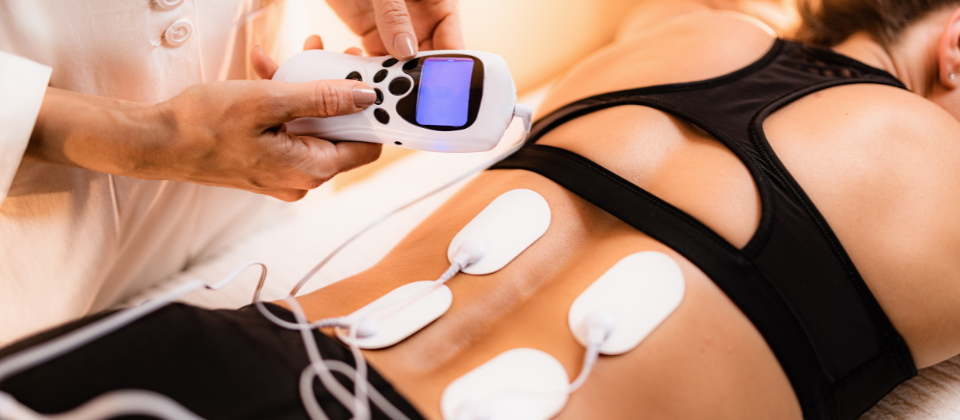 Person with 4 white adhesive patches on their back connected to a machine that is being held by someone else.