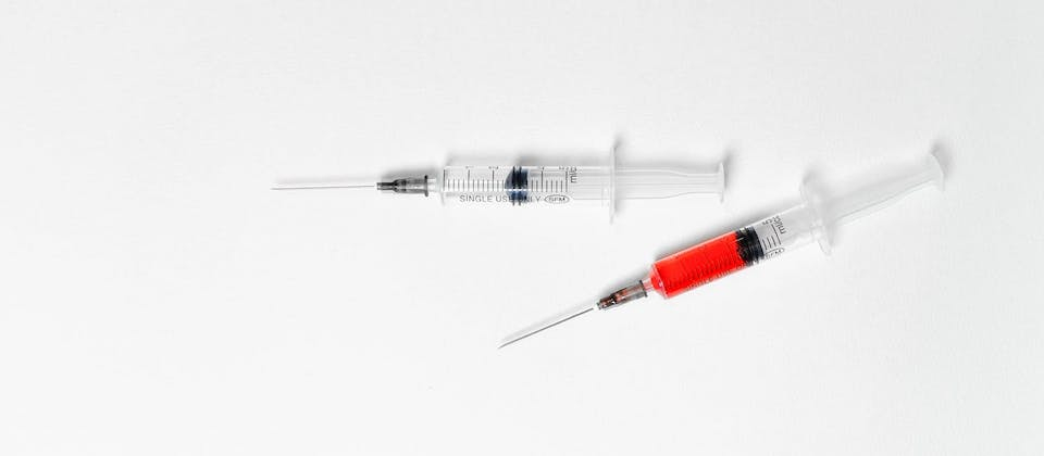 two syringes, one with clear fluid and the other with red fluid, on a white background