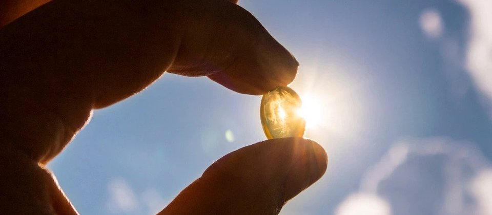 Translucent yellow pill held between two fingers up towards the sky