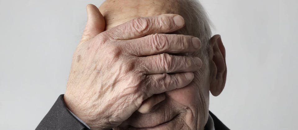 Elderly Man in Black Suit Jacket Covering His Eyes with His Hand