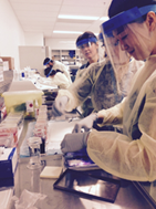 Doctors in training, wearing protective surgical gear, are dissecting a tissue specimen.