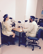 Two medical residents are each sitting at a microscope.
