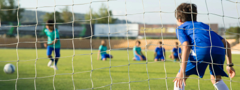 A young boy standing in front of a soccer goal.