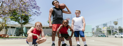 A basketball court scene with a young man and three kids posing.