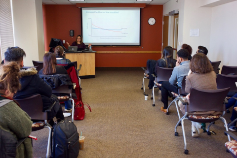 Students seated in rows facing a lecturer who is setting behind a desk.