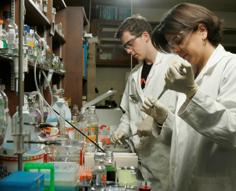 Two researchers in white lab coats surrounded by scientific equipment conducting an experiment