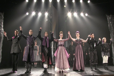Opera stage with a group of performers holding hands looking towards the audience
